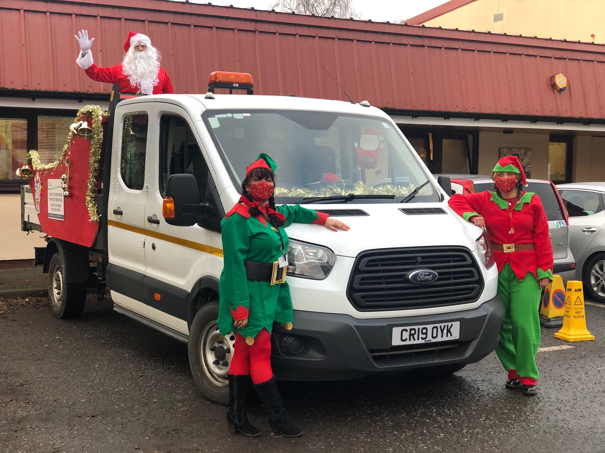 Image of Santa on top his a pick up truck with a red sleigh attached to the back with two elves at the front.