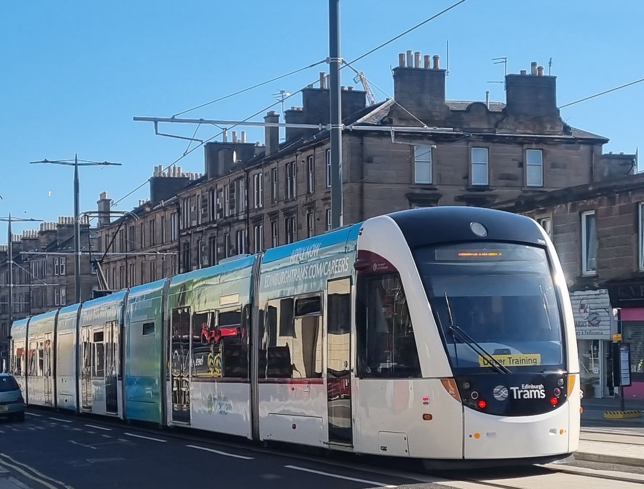 Photo of a tram during daytime testing on Croall Place, Leith Walk. A yellow driver training sign can be seen on the windscreen.
