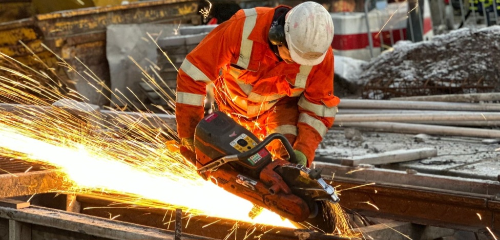 A photograph of a man in orange hi vis overalls welding new tram tracks at Picardy Place, with sparks flying